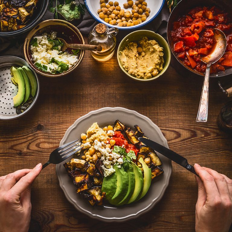 Eating healthy vegetarian meal in bowl with chick peas puree, roasted vegetables , red paprika tomatoes stew, avocado and seeds . Clean or dieting, vegetarian food concept